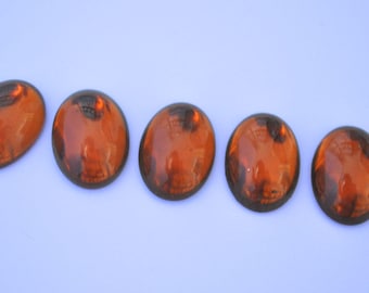 May include: Five round, amber-coloured glass stones arranged in a row on a light blue background.
