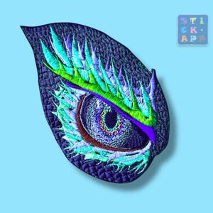 Könnte beinhalten: Gestickter Aufnäher mit einem detaillierten Augendesign in Blau-, Grün- und Lilatönen. Das Auge befindet sich auf einem dunkelblauen Hintergrund in Blattform. Der Aufnäher enthält den Text "STICK APP".
