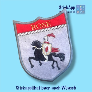 Könnte beinhalten: Ein schildförmiger Stickaufnäher mit grauem Hintergrund und einem roten oberen Band, das den gelben Schriftzug ROSE enthält. Darunter trägt ein schwarzes Pferd einen Ritter in silberner Rüstung mit roter Feder, der einen Schild mit rotem Emblem hält.