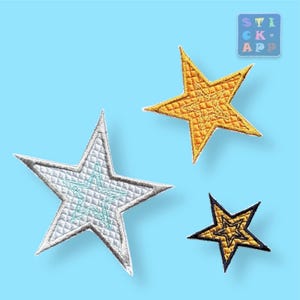 Könnte beinhalten: Drei gestickte Stern-Patches in verschiedenen Größen und Farben. Der größte Stern ist gelb, der mittlere Stern ist silber mit einem blauen Umriss und der kleinste Stern ist schwarz mit einem goldenen Umriss.