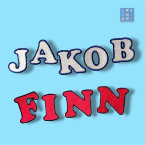 Könnte beinhalten: Zwei Reihen gestickter Aufbügler mit den Namen JAKOB und FINN. Die obere Reihe zeigt JAKOB in weißen Buchstaben mit dunkelblauen Rändern. Die untere Reihe zeigt FINN in roten Buchstaben mit schwarzen Rändern. Ein kleines Logo zeigt den Text STICK APP.