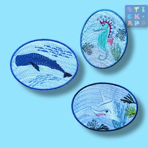 Könnte beinhalten: Drei gestickte Aufnäher mit maritimen Motiven. Einer zeigt einen Blauwal, ein anderer ein Seepferdchen mit roten und türkisfarbenen Details und der dritte einen Marlin. Jeder ovale Aufnäher hat einen blauen Rand, vor einem hellblauen Hintergrund.