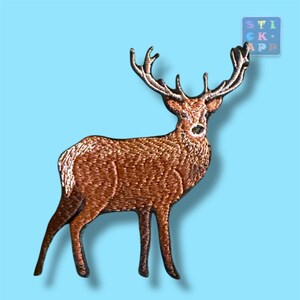 Könnte beinhalten: Ein gestickter Aufnäher, der einen braunen Hirsch mit großem Geweih im Profil zeigt. Der Hirsch hat eine strukturierte Stickerei in hellen und dunklen Brauntönen. Ein kleines quadratisches Logo in der oberen rechten Ecke enthält den Text STICK APP.