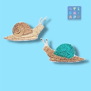 Könnte beinhalten: Zwei gestickte Schneckenaufnäher. Eine Schnecke hat ein braunes Gehäuse, die andere ein türkisfarbenes Gehäuse. Beide Schnecken haben beige Körper und Fühler. Die Aufnäher befinden sich auf einem hellblauen Hintergrund. Der Text "STICK APP" befindet sich in einem Quadrat oben rechts.