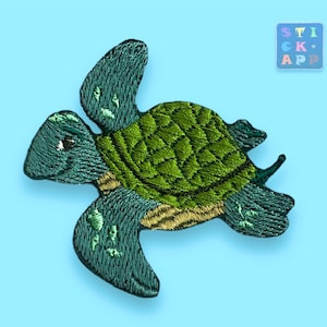 Könnte beinhalten: Grüne und blaue gestickte Meeresschildkröten-Aufnäher. Die Schildkröte schwimmt mit ausgestreckten Flossen.