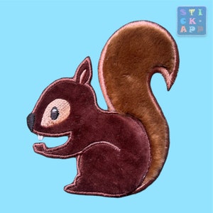 Könnte beinhalten: Ein braunes Plüsch-Eichhörnchen mit einem flauschigen Schwanz, das auf einem hellblauen Hintergrund sitzt.