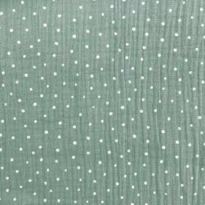 May include: Close-up of a textured fabric in a muted green color, scattered with small, evenly spaced white polka dots. The fabric has a slightly crinkled appearance, suggesting a soft, breathable material. Ideal for apparel or home decor.