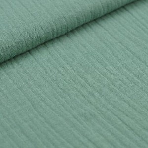 May include: Close-up of a folded piece of sage green fabric. The fabric has a textured, ribbed appearance, with vertical lines running across the material. The fabric appears soft and lightweight, suitable for various sewing projects.