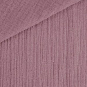 May include: Close-up of a dusty rose-colored fabric with a crinkled texture. The fabric is folded diagonally, revealing a layered effect. The material has a soft, matte appearance, suitable for various textile projects.