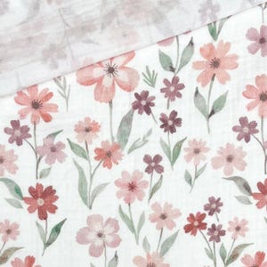 May include: White fabric with a watercolor floral pattern. The design features various sizes of flowers in shades of pink, red, and purple, with green leaves. The fabric is folded over, revealing a similar, lighter floral pattern.