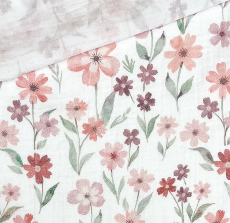 May include: White fabric with a watercolor floral pattern. The design features various sizes of flowers in shades of pink, red, and purple, with green leaves. The fabric is folded over, revealing a similar, lighter floral pattern.