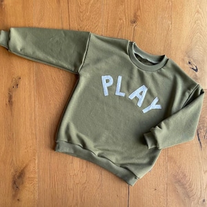 May include: A green sweatshirt with the word "PLAY" in white letters on the front.