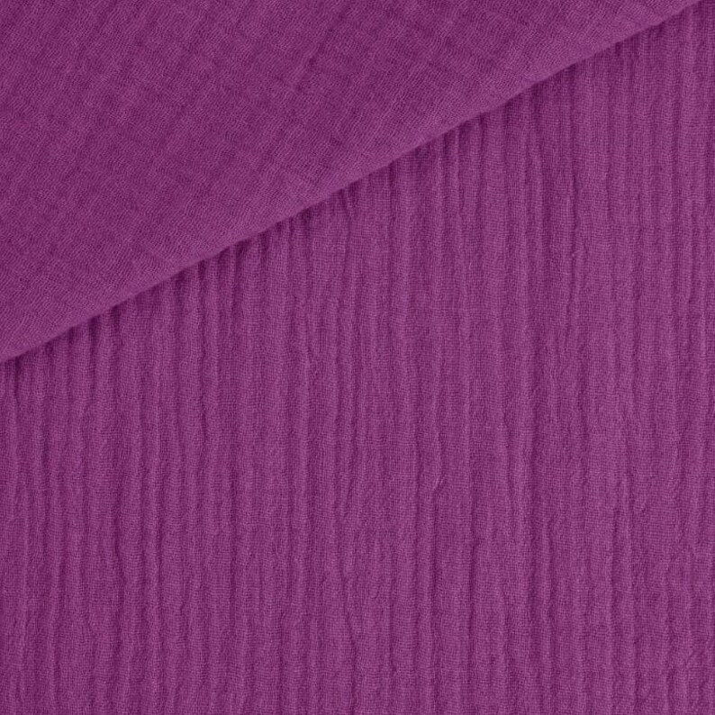 May include: Close-up of a textured, purple fabric. The fabric is folded diagonally, revealing a layered effect. The material has a crinkled, ribbed appearance, with vertical lines running down the surface. The color is a vibrant, deep shade of purple.