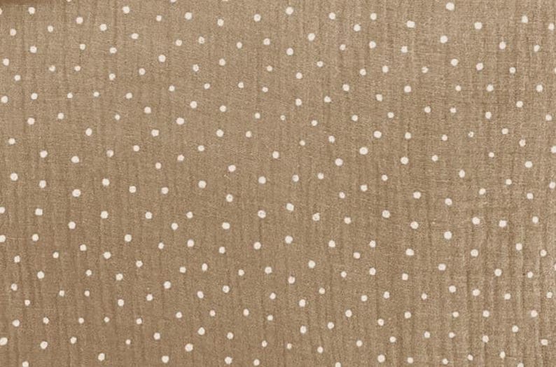 May include: Close-up of a tan fabric with a repeating pattern of white polka dots. The fabric has a slightly textured appearance, with the dots irregularly spaced across the surface. The overall effect is a simple, yet visually interesting design.