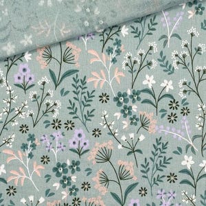 May include: A close-up of a fabric with a floral pattern. The fabric is a light green color with a repeating pattern of flowers and leaves in shades of white, pink, purple, and green. The fabric is folded over in the upper left corner.