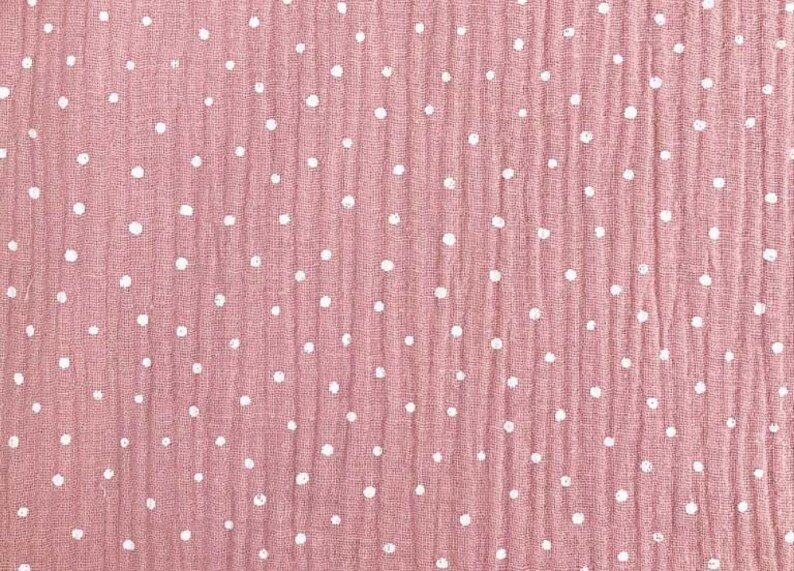 May include: A close-up of a dusty rose fabric with a crinkled texture. The fabric is dotted with evenly spaced white polka dots. The material appears to be a lightweight cotton or linen, suitable for clothing or home decor.