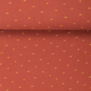 May include: Close-up of a terracotta-colored fabric with a repeating pattern of small, golden yellow half-circle shapes. The fabric is folded, showing a textured surface. The design is evenly spaced across the material, creating a consistent visual texture.