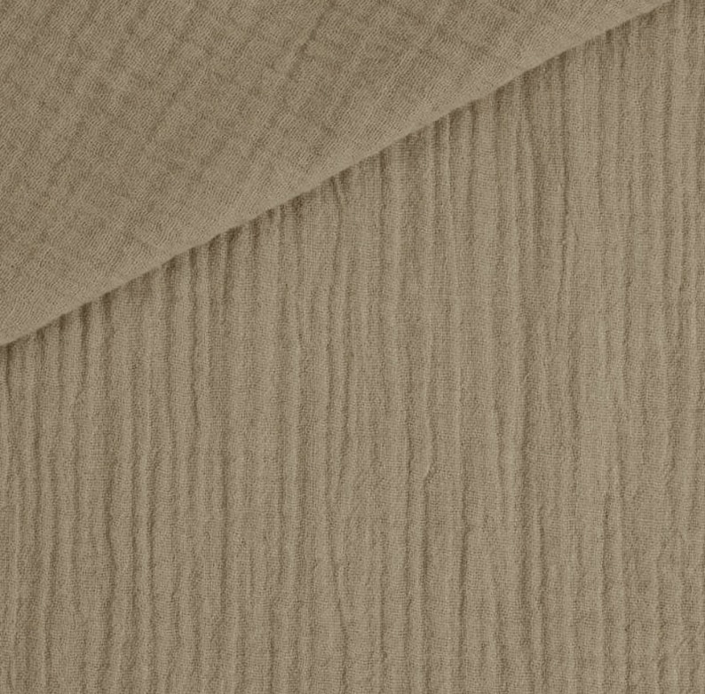 May include: Close-up of a tan-colored fabric with a crinkled texture. The fabric is folded over, revealing a layered effect. The material has a soft, natural appearance, suitable for various textile projects.