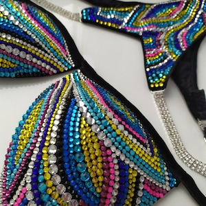 May include: A black bikini top and bottom with a colorful geometric design made of rhinestones. The design features blue, yellow, pink, and clear rhinestones.