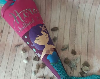 Pode incluir: Um cone escolar rosa e azul com um design de sereia. O cone tem uma inscrição de glitter prateado que diz "Horaz Schulkind 2023". A sereia tem cabelo roxo, um top azul e uma cauda turquesa com lantejoulas.