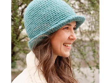 May include: A teal blue crocheted hat with a wide brim. The hat is worn by a person with long brown hair. The hat is made with a textured stitch. The image includes the text "DROPS DESIGN. www.garnstudio.com".