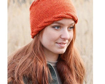 May include: An orange knitted headband with a textured design. The headband is worn on the head. The image also includes the text "DROPS DESIGN" and the website address "www.garnstudio.com".