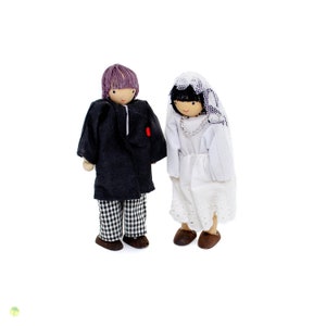 May include: A pair of wooden dolls dressed in wedding attire. The groom is wearing a black suit with a white and black checkered pattern on the pants. The bride is wearing a white dress with a lace trim and a white veil.