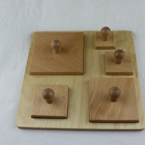 May include: Wooden puzzle board with five square blocks of varying sizes, each topped with a small, rounded knob. The blocks are arranged on a light-colored wooden base. The puzzle is designed for early childhood development.