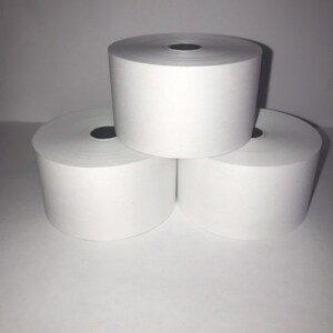 Puede incluir: Tres rollos de papel térmico blanco para recibos, apilados uno encima del otro.