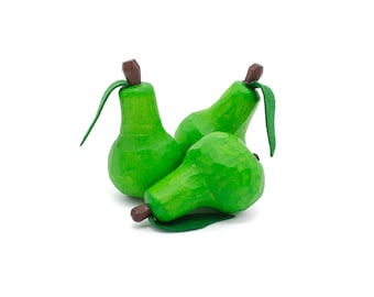 May include: Three hand-carved wooden pears in varying positions. Each pear is painted a vibrant green with a brown stem and a green leaf. The pears are arranged on a white background, showcasing their detailed craftsmanship.