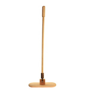 Könnte beinhalten: Ein Holzmopp mit einem langen, hellfarbigen Stiel und einer rechteckigen Basis. Der Griff ist mit einem Metallgelenk an der Basis befestigt. Der Moppkopf besteht ebenfalls aus hellfarbenem Holz. Der Mopp ist zum Reinigen von Böden bestimmt.