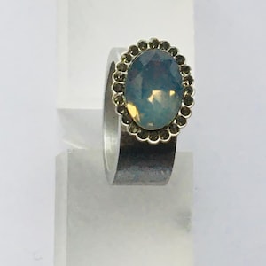 May include: A silver ring with a large oval-shaped blue gemstone surrounded by a halo of smaller black gemstones.