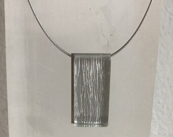 Chain made of aluminiumin connection with silver threads behind glass