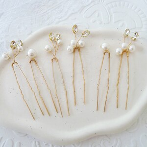 May include: Set of six gold hair pins with pearl and crystal accents. Each pin features a delicate branch design with small pearls and clear crystals.