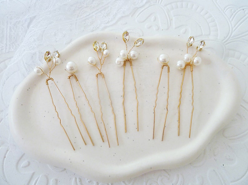May include: Set of six gold hair pins with pearl and crystal accents. Each pin features a delicate branch design with small pearls and clear crystals.