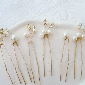 May include: Six gold hair pins with pearl and rhinestone accents. Each pin features a delicate floral design with three pearls and a rhinestone.