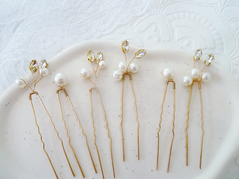 May include: Six gold hair pins with pearl and rhinestone accents. Each pin features a delicate floral design with three pearls and a rhinestone.