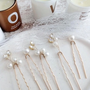 May include: Six gold hair pins with pearl and crystal accents. The pins are arranged on a white surface.