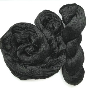 Può includere: Tre matasse di filato nero su sfondo bianco. Due sono avvolte strette, una sciolta. Il filato sembra morbido, ideale per progetti di maglia o uncinetto. Il filato è probabilmente venduto a peso, come in grammi.