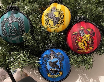 Puede incluir: Cuatro adornos navideños redondos con escudos de las casas de Hogwarts: Slytherin, Hufflepuff, Gryffindor y Ravenclaw. Cada adorno tiene un ribete de cuerda negra y un lazo plateado para colgar. Se exhiben sobre agujas de pino verdes.