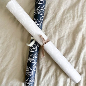 Puede incluir: Dos rollos de papel de regalo con un patr&oacute;n de hojas blancas sobre fondo negro y un patr&oacute;n de hojas blancas sobre fondo blanco.