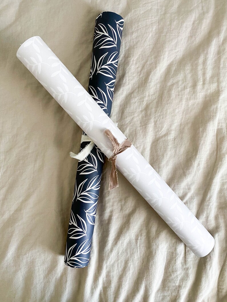 Puede incluir: Dos rollos de papel de regalo con un patr&oacute;n de hojas blancas sobre fondo negro y un patr&oacute;n de hojas blancas sobre fondo blanco.