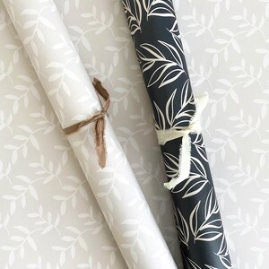 Puede incluir: Dos rollos de papel de regalo con un patr&oacute;n de hojas blancas. Un rollo es blanco con hojas blancas y el otro rollo es negro con hojas blancas.