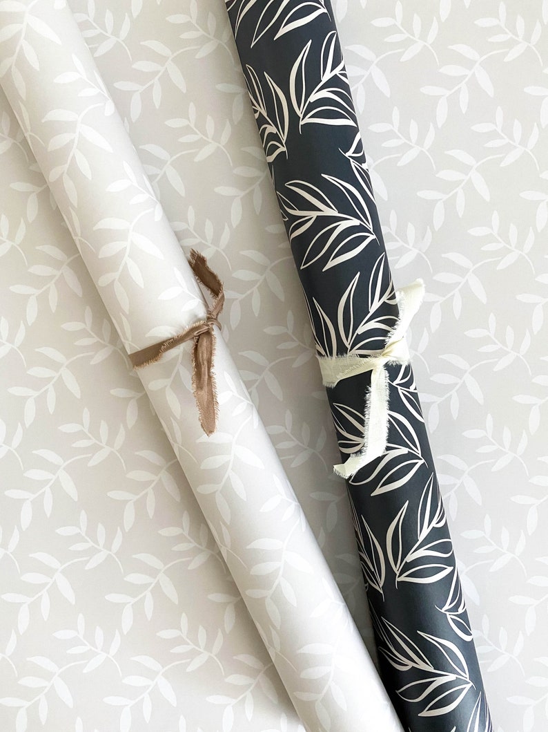 Puede incluir: Dos rollos de papel de regalo con un patr&oacute;n de hojas blancas. Un rollo es blanco con hojas blancas y el otro rollo es negro con hojas blancas.