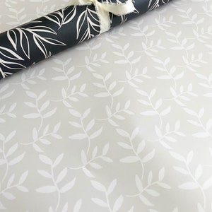 Puede incluir: Un rollo de papel de regalo negro y blanco con un patr&oacute;n de hojas. El papel est&aacute; enrollado y atado con una cinta blanca.