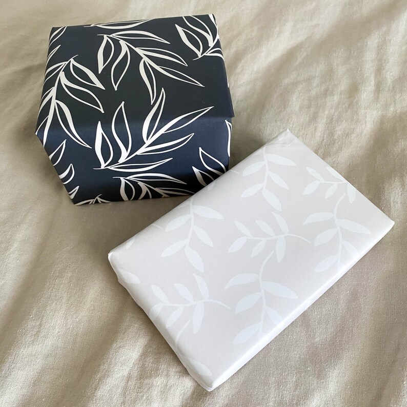 Puede incluir: Dos cajas de regalo con diferentes patrones de hojas. Una caja es negra con hojas blancas, la otra es blanca con hojas negras.