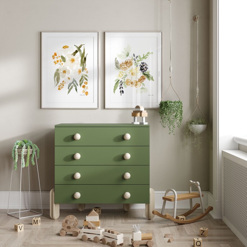 May include: A green dresser with four drawers and white knobs, flanked by framed floral art prints. A wooden rocking horse and toy train sit on the floor, creating a nursery or children's room theme. Hanging planters add a touch of greenery.