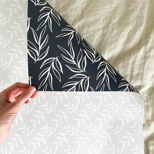 Puede incluir: Dos rollos de papel tapiz blanco y negro con un patr&oacute;n de hojas simple. El papel tapiz se muestra parcialmente desenrollado, revelando los patrones blanco y negro.