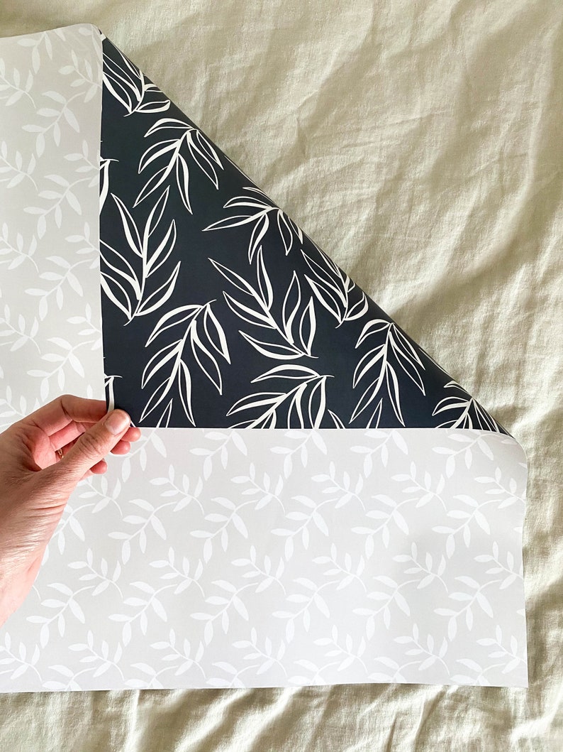 Puede incluir: Dos rollos de papel tapiz blanco y negro con un patr&oacute;n de hojas simple. El papel tapiz se muestra parcialmente desenrollado, revelando los patrones blanco y negro.