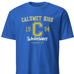 May include: A royal blue t-shirt with the text "CALUMET HIGH" in yellow, a large yellow "C", and the numbers "1984". Below, it reads "Wolverines" and "Calumet, CO".